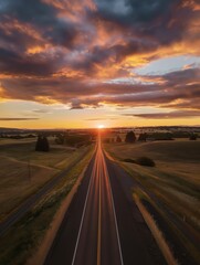 Fototapeta premium Vertical shot of long road winding through rural Washington landscape at sunset. Hills, mountains, forests surround road. Clouds reflect in sky, creating beautiful evening scene. Trees line road,