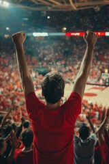 White man in vibrant red shirt stands in center of noisy basketball game, his arms raised high and hands clasped together, surrounded by blur of colors and shapes as fans cheer on their team.