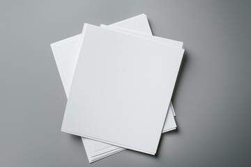 Blank paper sheets on grey background in top view. Mock-up of brochure layout with empty pages for design and copy. Paper stack on office desk for business and marketing purposes.
