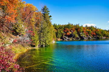 Naklejka premium Stunning autumnal views of the lovely Pink Lake against the change of colours of the boreal forest from green to deep orange as Fall sets in at Gatineau Park,Quebec,Canada