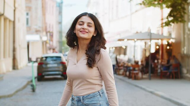 Portrait of happy Indian young woman turning smiling friendly glad expression looking at camera dreaming resting relaxation feel satisfied good news outdoor. Hispanic girl walking on urban city street
