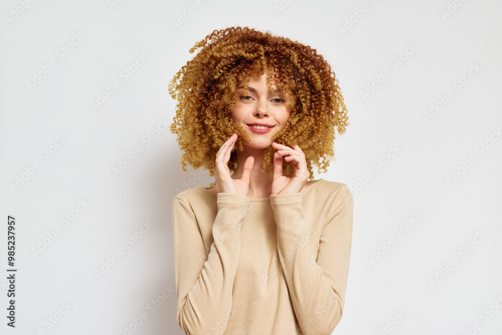 Wall mural smiling woman with curly hair in neutral colored outfit against white background, displaying joy and