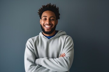 Obraz premium Young African American man with beard smiles, crosses arms, and looks at the camera with confidence. Casual sweatshirt, happy expression, and friendly pose.