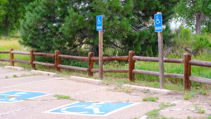 Accessible parking spaces marked by blue signs and painted symbols of handicapped parking spots on asphalt surface in a nature park parking lot. Accessibility and inclusion concept.