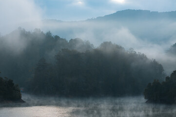 Foggy lagoon at dawn in diffuse blue tones that invite mystery and intrigue Beautiful colors blurred between the clouds with a forest on an island on the shore of the turquoise waters and mountain in 