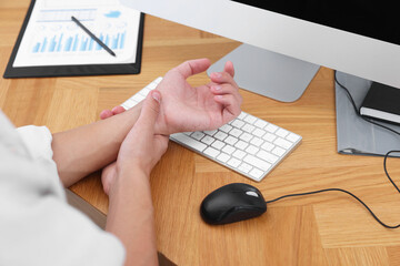 Man suffering from pain in wrist while working on computer at wooden table, closeup. Carpal tunnel...