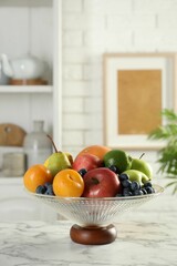 Glass vase with different fresh fruits on white marble table