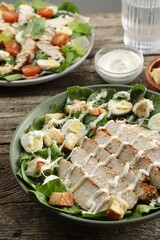 Delicious Caesar salad with chicken on wooden table, closeup