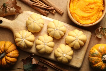 Raw pumpkin shaped buns and ingredients on brown table, flat lay