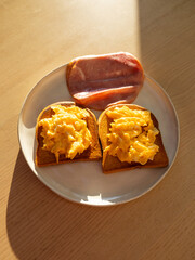 Breakfast plate of scrambled eggs, toast, and ham.