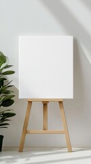 Empty canvas on wooden easel near a green plant, bright interior.