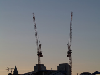Fototapeta premium Two Near Silhouette Cranes Standing Above Building With Blue Sky