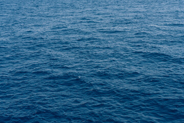 Serene view of the calm ocean water, natural texture and color of the sea under clear skies. Small ripples on still water surface. Summer daylight