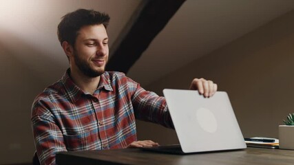 End of video conference. Young man waving hand good bye to laptop screen, saying goodbye to chat colleagues and closing laptop, sitting at workplace at home office
