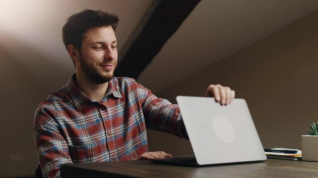 End of video conference. Young man waving hand good bye to laptop screen, saying goodbye to chat colleagues and closing laptop, sitting at workplace at home office