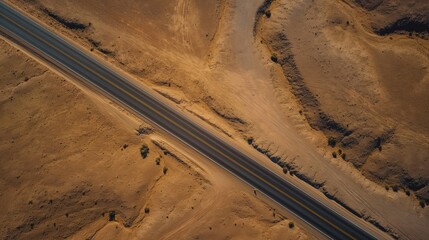 Aerial top view of winding road through vast dry desert landscape with rocky hills, sandy terrain. Road narrow path through rural area with scattered stone structures in background. Desert landscape