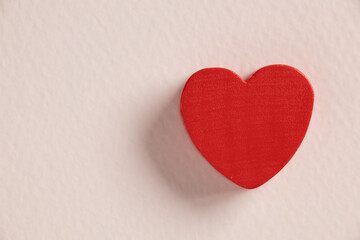 Red valentines heart made of wood against a pink background.