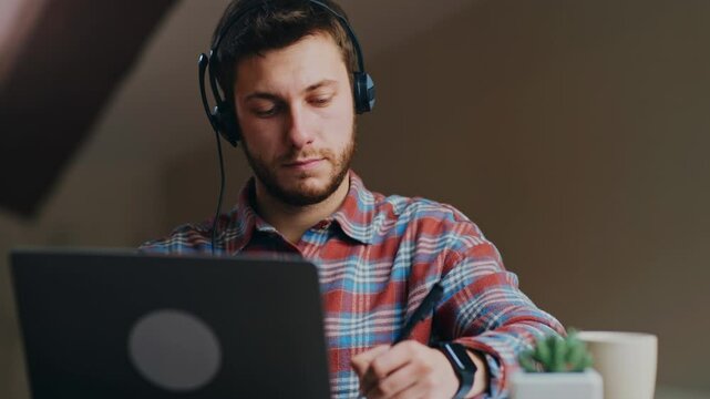 New normal and remote learning. Young man in headset watching online webinar and making notes, studying remotely at home