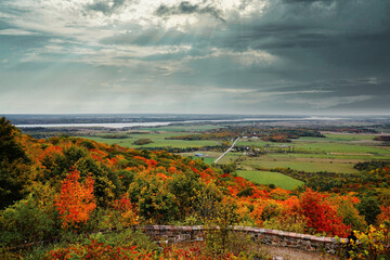 Dark rain clouds hover above a panoramic scene of the farms,Ottawa river and city from the Champlain look out point with a vivid range of fall colours visible at  Gatineau Park,Quebec,Canada