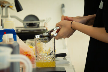 Women barista extracting lemon juice to glass using a lemon squeezer, in a cafe environment. Faceless portrait