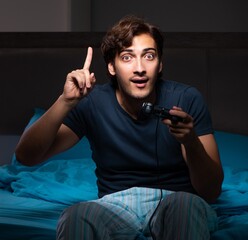 Young man playing computer games at night in bed