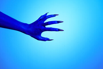 Obraz premium A blue witch hand with sharp red nails, set against a backdrop of blue fire. This eerie figure embodies demonic, ghostly, and zombie elements, perfect for Halloween horror and fantasy settings.