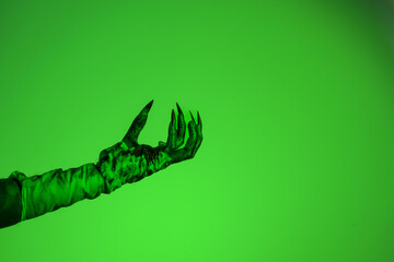 A bloodied witch hand wrapped in bandages, set against a green fire background. This demonic hand...