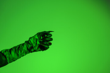 A bloodied witch hand wrapped in bandages, set against a green fire background. This demonic hand...