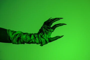 A bloodied witch hand wrapped in bandages, set against a green fire background. This demonic hand...