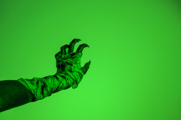 A bloodied witch hand wrapped in bandages, set against a green fire background. This demonic hand...