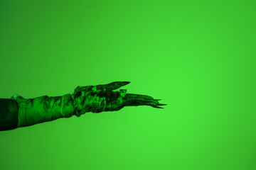 A bloodied witch hand wrapped in bandages, set against a green fire background. This demonic hand...