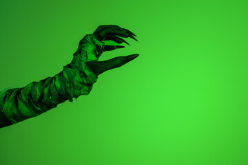 A bloodied witch hand wrapped in bandages, set against a green fire background. This demonic hand...