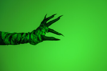 A bloodied witch hand wrapped in bandages, set against a green fire background. This demonic hand...