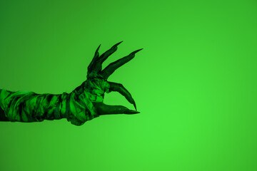 A bloodied witch hand wrapped in bandages, set against a green fire background. This demonic hand...