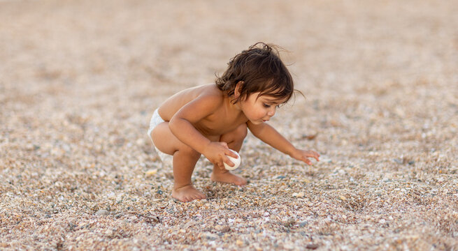 infant wearing only a nappy squatting down to look at coarse beach sand