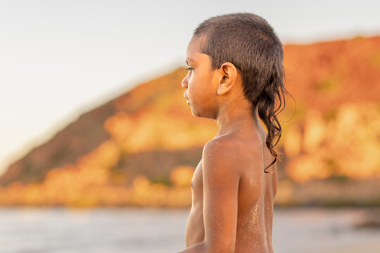 kid with rat tail haircut looking out to beach in profile against blurry landscape