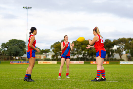 three young women training for australian rules football on green turf oval