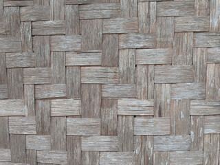 A close-up of a weathered bamboo woven wall, showcasing the intricate pattern and natural texture of the bamboo. The wall has a rustic and traditional feel.