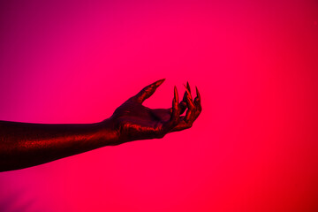 A witch hand with long nails appears against a red fire background, evoking a demonic, monstrous...