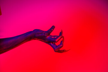 A witch hand with long nails appears against a red fire background, evoking a demonic, monstrous...