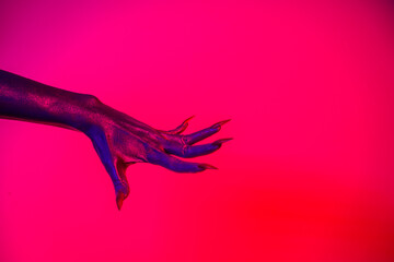 A witch hand with long nails appears against a red fire background, evoking a demonic, monstrous...