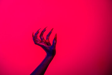 A witch hand with long nails appears against a red fire background, evoking a demonic, monstrous...