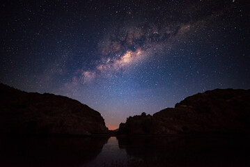 Silhouettes of two mountains under a night sky filled with stars.