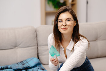 Obraz premium Young woman holding a mask nebulizer inhaling fumes medication into lungs. Caucasian sick lady inhaling through inhaler mask at home. Self treatment of the respiratory tract using inhalation nebulizer