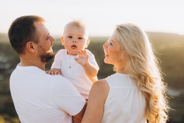 Happy Family Enjoying Outdoor Moments with Their Baby at Sunset in Scenic Nature