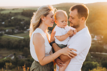 Fototapeta premium Happy Family Bonding Outdoors in Summer Sunset with Parents Holding Baby