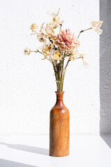 Dried flowers in brown vase casting a shadow on white textured wall.