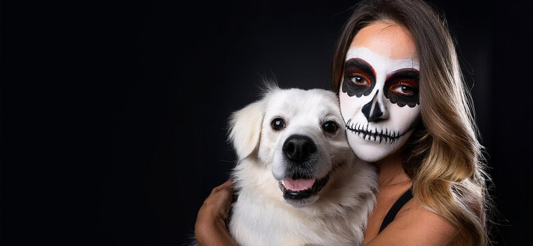 Donna con viso disegnato come un teschio mentre abbraccia un cane. sfondo nero
