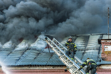 Two firefighters are on a ladder, one of them is sitting on it