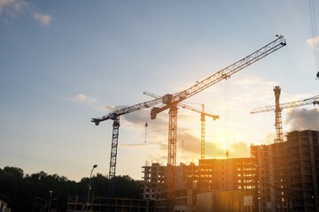 Cranes lift materials at a bustling construction site as the sun sets, signaling the end of a productive day in building development